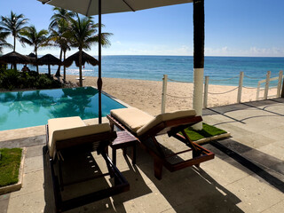 Relaxing sun loungers with umbrellas in a pool and beach of a large Caribbean luxury resort hotel, with a beach of fine white and golden sand with crystal clear turquoise water in the background.
