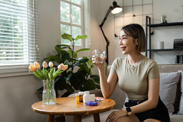 Young Woman Taking Medication at Home, Sitting on Sofa with Glass of Water, Surrounded by Healthcare Products and Natural Light