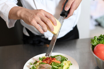 厨房でグレーターでチーズを削る調理師の手元