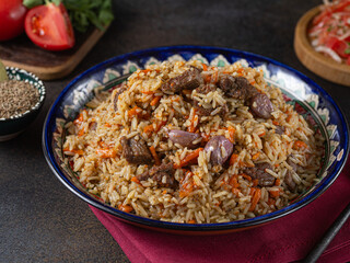 National Uzbek pilaf with meat in a cast-iron skillet, on a wooden table. The concept of oriental cuisine