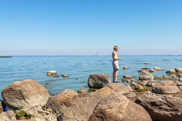 Boy 8 years old standing on rocks and looking at sea. Rear view.