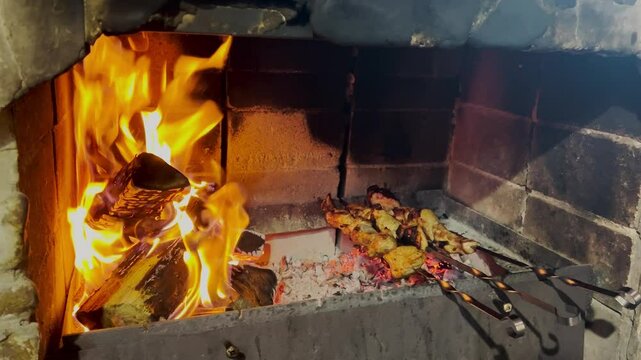 Burning firewood in fire-box of fireplace with cooking meat. Marinated skewers or shish kebab.