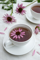 Herbal tea in white cups, fresh flowers of echinacea on a marble background. Side view. 