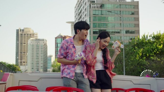 asiatic young happy couple travel together on open bus touring a modern capital city while dancing listening to pop summer hit and making soap bubble with a toy gun 