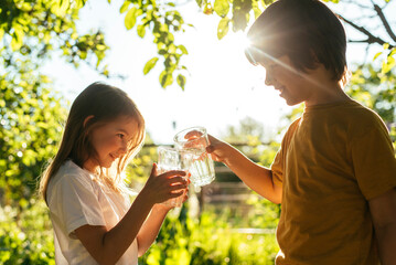 Fototapeta premium A boy and a girl drink water from a glass in nature on a sunny day