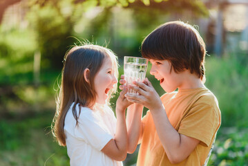 Beautiful children hold a glass of water in their hands in nature. Healthy lifestyle concept