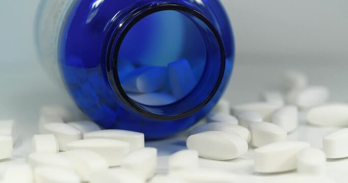 Big white pills scattered on table. Overdose. Open blue container for nutritional supplements lies on table. In reality these are biologically active sulfur pills in dosage of 1500 mg, MSM for joints