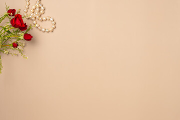 Beige background with red roses and pearls. Flat lay, top view. Copy space
