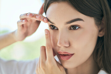 Woman inserting a contact lens into her eye, close-up. Concept of eye care, vision correction, and...