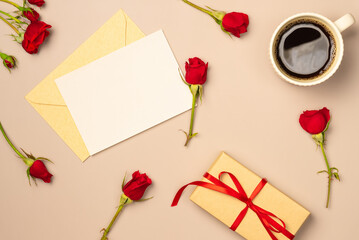 Paper blank sheet with red roses, mug of coffee and gift box on beige background from above. Greeting card. Space for text