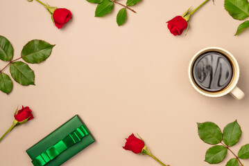 Frame of red roses, gift box and mug of coffee on beige background . Flat lay, top view. Copy space