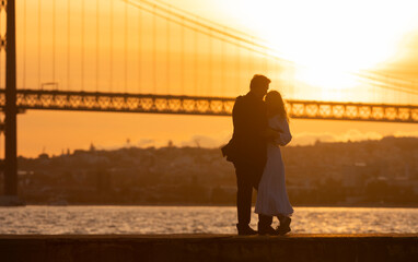 Fototapeta premium A couple is kissing in front of a bridge with the sun setting in the background