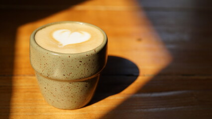 a cup of hot cappuccino on a wooden table with a space to the right of the cup
