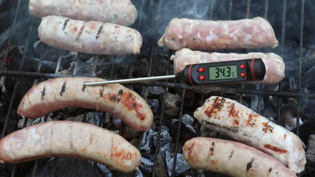Person checking grilled sausages on barbecue with digital thermometer with Celsius scale. It shows temperature below the safe cooking threshold for pork meat signaling a potential risk of foodborne il