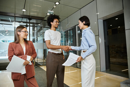 Three colleagues chat and shake hands in a modern office lobby.