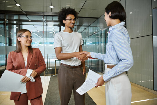 Three colleagues chat and shake hands in an office lobby.