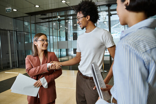 Three colleagues smile and chat in an office lobby.