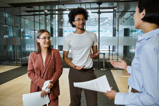Three colleagues stand and converse in an office lobby.