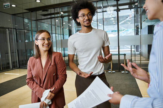 Three colleagues chat amicably in an office lobby, showcasing diversity - Powered by Adobe