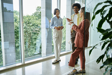 Three colleagues, including one with a prosthetic leg, stand near a window and chat while holding coffee cups.