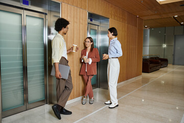 Three diverse colleagues chat and laugh in a modern office lobby, one woman wearing a prosthetic...