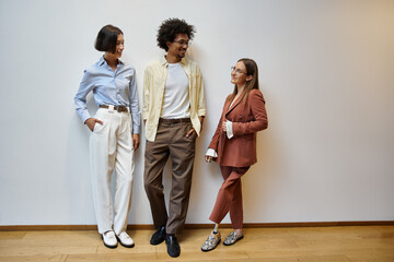 Three colleagues, including a woman with a prosthetic leg, stand against a white wall and chat in a...