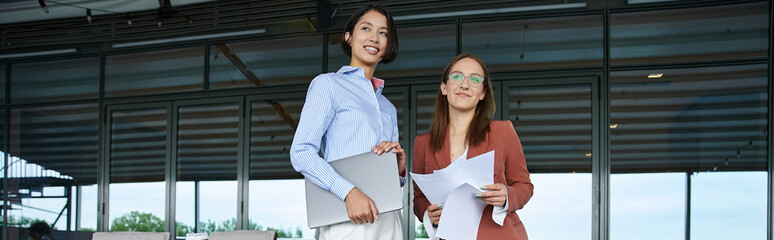Two colleagues stand on a modern rooftop terrace, engaging in a friendly conversation.