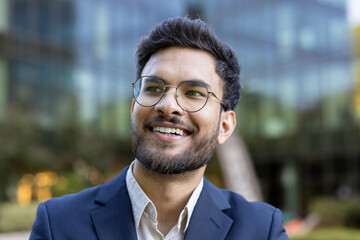 Smiling young professional wearing glasses in business attire. Outdoor portrait taken in urban business district. Perfect for career, corporate, and business themes.