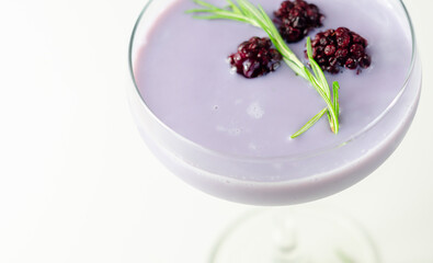 A glass of purple liquid with blackberries floating on top