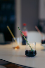 A glass of soda with a straw in the foreground with additional glasses with straws in the background