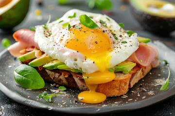 A delicious sandwich featuring a fried egg with a runny yolk on top of avocado slices and ham, garnished with fresh herbs, creating a perfect meal for any time of day.