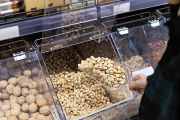 A hand reaching for pistachios in a bulk bin at a grocery store. This image reflects the eco-conscious trend of purchasing bulk foods to minimize packaging waste.