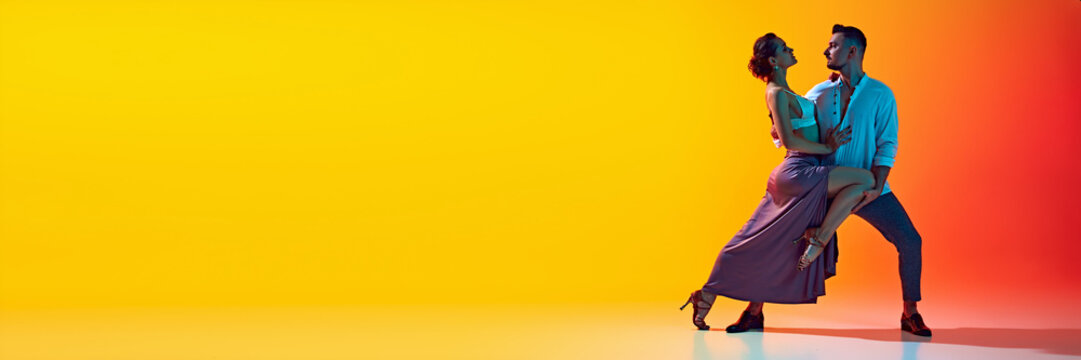 Bachata dance class. Couple, man and woman in dynamic pose highlighting passion of bachata dance against gradient yellow orange background in neon. Concept of dance, performance, art, entertainment