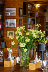 Yellow flowers stand in a transparent vase on the dining table with a table setting for dinner. Dining table against a background of a wooden wall with vintage photos
