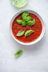 Bowl of tomato soup on a light-grey granite background, vertical shot with space, top view