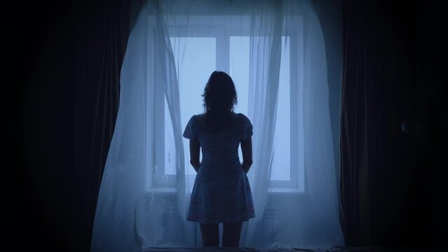 unrecognizable black dark silhouette of woman standing looking at window, mood depression sadness loneliness emotion. Mystery Adult Girl back rear view. wind blows curtains fly waving white fabric 4k