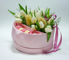 Pink box with tulip flowers and sweet macarons on a white background