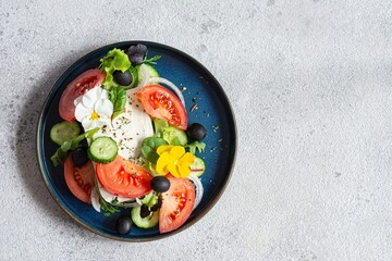 Appetizing salad with feta cheese, fresh vegetables (tomatoes, cucumbers, onions), crispy lettuce, microgreens and violet flowers. Non-standard serving of Greek salad.