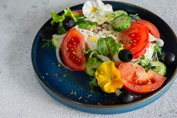Appetizing salad with feta cheese, fresh vegetables (tomatoes, cucumbers, onions), crispy lettuce, microgreens and violet flowers. Non-standard serving of Greek salad.