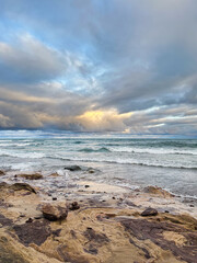 Beautiful Lake Superior landscape, morning light in a cloudy sky over teal blue waters and waves crashing on the rocky lakeshore