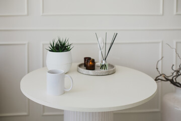 Still life with white mug, aromatic sticks and candles on a table in a cozy living room.