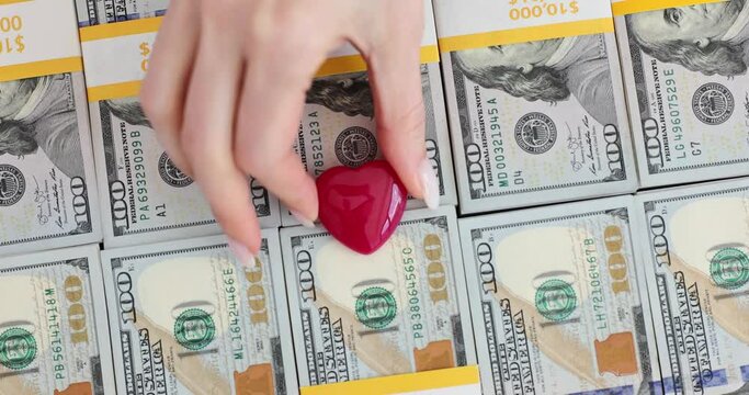 Woman places red heart on packed stacks of dollar banknotes