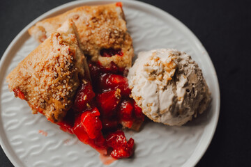 pieces of pie with strawberries and ice cream on a plate, dark background, closeup