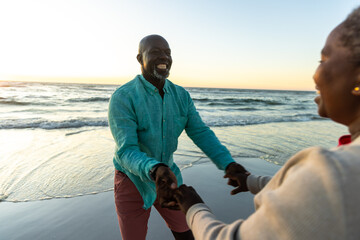 Fototapeta premium Senior African American couple enjoys a playful moment on the beach, with copy space