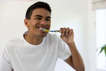 Young biracial man brushing teeth in a bright home bathroom