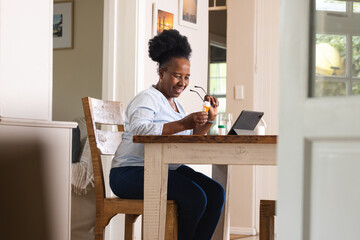 Happy senior african american woman holding pills and using tablet at home
