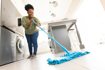Happy senior african american woman cleaning floor with mop at home