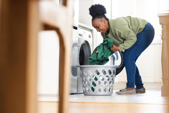 Happy senior african american woman doing laundry in kitchen at home