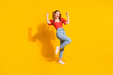 Full size photo of pretty young girl winning raise fists wear trendy red outfit isolated on yellow color background