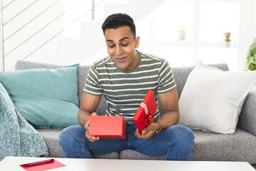 Middle Eastern man opens a gift at home during a video call, with copy space